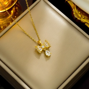 Golden bow necklace with zircon drop pendant displayed in a luxury textured gift box