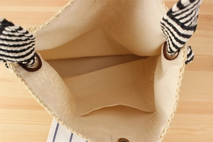 Detail view of the interior fabric lining and small inner pocket of the woven straw tote bag