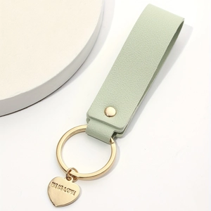 Close-up of light green leather keychain with golden heart pendant engraved with HE IS LOVE
