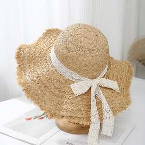 Detail of raffia sun hat with wavy brim and white lace ribbon on a wooden stand