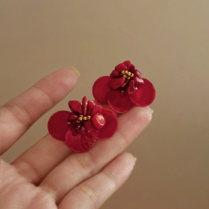Detail view of deep red flower stud earrings with gold beads and resin petals