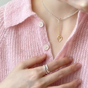 Close-up of minimalist silver wave ring and gold heart pendant necklace on model