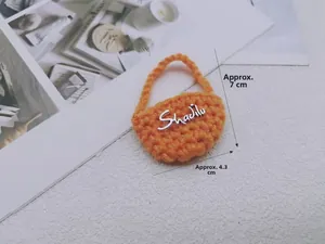 Dettaglio mini borsa all'uncinetto arancione con dimensioni 7cm x 4,3cm e logo metallico