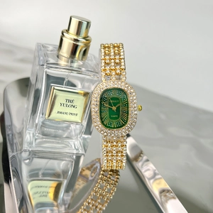 Detailed shot of golden rhinestone watch with green oval dial next to a perfume bottle