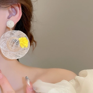 Close-up of woven straw hat earrings with yellow floral accents for summer style
