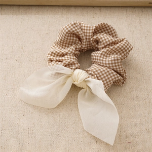 Detail of plaid fabric scrunchie in brown and white with a soft white chiffon bow tie