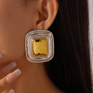 Macro detail of mixed-metal geometric stud earrings with hammered texture on earlobe
