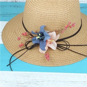 Dettaglio cappello di paglia beige con decorazioni floreali e bacche rosse su legno rigato