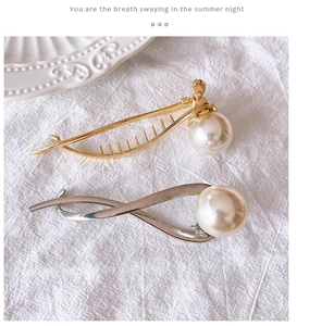Detail of elegant gold and silver metal hair claws featuring large white pearls on fabric