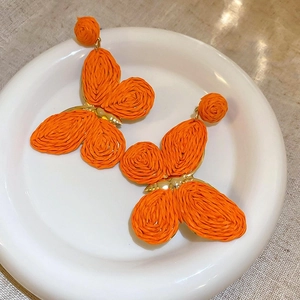 Detailed view of orange woven butterfly earrings on a ceramic tray for a beach look