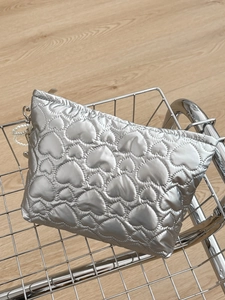 Detail view of silver heart-quilted makeup bag with elegant pearl charm in a metal basket