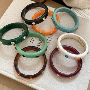 Stack of colorful acrylic resin bangles with inlaid rhinestones on a beige textured book