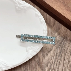 Close-up of a rectangular silver metal hair clip with light blue rhinestones on a tray