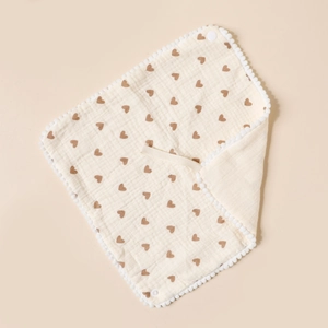 Detail of soft cotton baby bib with brown heart print and white pompom trim