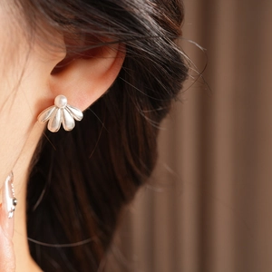 Macro view of a silver floral stud earring with a white pearl on a model's ear
