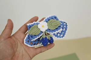 Detail of hand-crocheted blue bow hair clip with white flower and strawberry charms