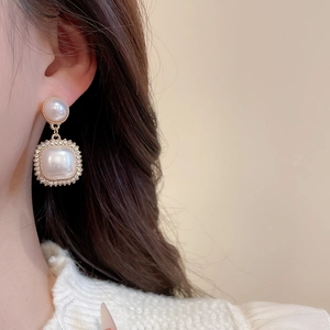 Close-up of elegant pearl drop earrings with crystal-encrusted square charm on model