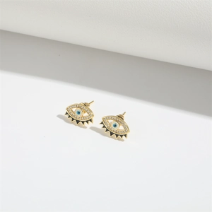Close-up of golden evil eye stud earrings with blue stones and zircon inlay