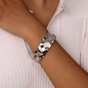 Close-up of a silver-colored C-shaped wide cuff bracelet with wavy hammered metal texture