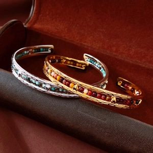 Macro detail of gold plated open cuff bracelet with colorful gemstone beads and heart relief