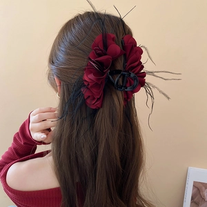 Detail showing dark red fabric floral hair claw with black feathers on brunette hair