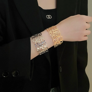 Detail of wide cut-out floral pattern metal bangle in gold and silver finishes