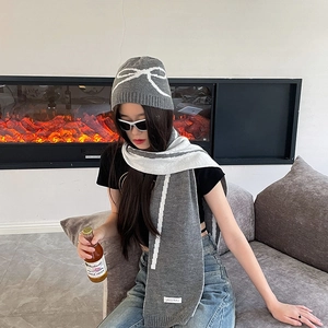 Detail of grey bow jacquard knit hat and striped scarf set on female model indoors