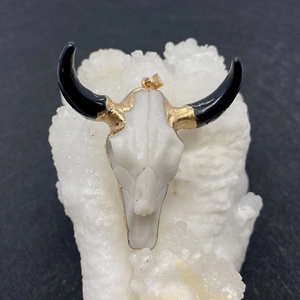 Cow skull pendant with black horns and golden accents on a white crystal cluster base