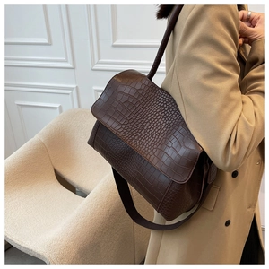 Detail view of a dark brown crocodile pattern shoulder bag with a wide strap on a model