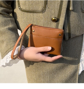 Brown leather coin purse with wrist strap and metal studs details held by a model