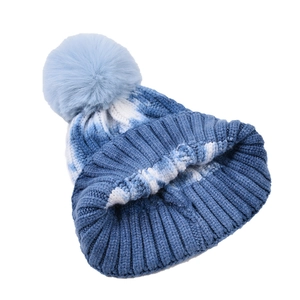 Tie-dye blue and white winter knit hat with a soft faux fur pom-pom on plain background