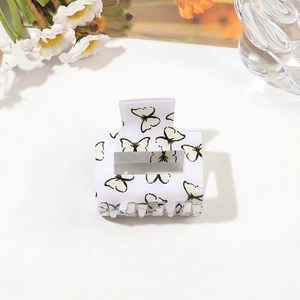 Close-up of a white square hair claw clip featuring yellow butterfly prints and metal spring