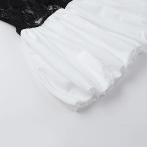 Dettaglio ravvicinato delle cuciture in pizzo nero e del tessuto plissettato bianco dell'abito