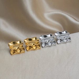 Macro shot of gold and silver wavy geometric earrings on elegant beige silk fabric