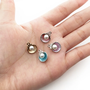 Close-up of four colorful seashell charms with pearls held in a hand for DIY jewelry