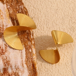 Macro view of golden twisted fan-shaped earrings on natural bark and beige surface