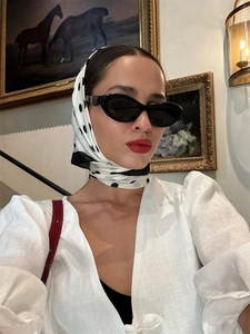 Detailed view of white linen V-neck top paired with polka dot headscarf and cat-eye sunglasses