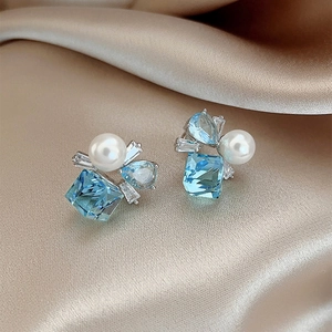 Macro shot of square blue crystal stud earrings with pearls on champagne silk background