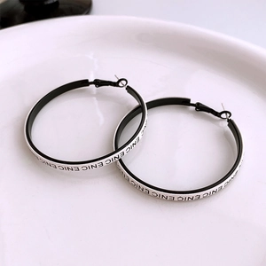 Detailed view of large black and white hoop earrings with ENIC letters on a white ceramic plate