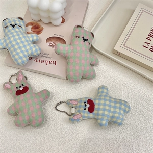 Detailed view of plush checkered bear and rabbit charms with metal chains on a white tray