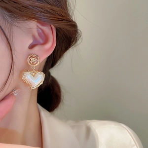 Close-up of vintage heart earrings with pearl inlay and golden textured edges on a model
