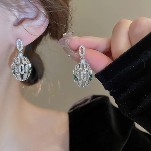 Macro shot of silver C-shaped snake stud earrings with zircons and green stone eyes