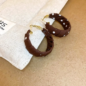 Close-up of brown polka dot fabric wrapped hoop earrings with gold metal accents