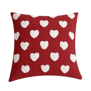Close-up of red tufted pillow showing white embroidered heart patterns and soft texture