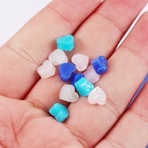 Detailed close-up of 8mm heart-shaped resin opal beads in white and blue on a palm