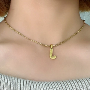 Dettaglio della collana dorata con pendente lettera L e superficie strutturata
