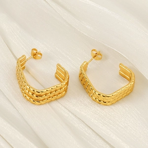 Three-layer braided gold titanium steel hoop earrings on elegant silk fabric background