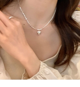 Close-up of minimalist silver heart pendant necklace and matching ring on model