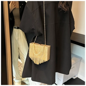 Detail of a luxury gold evening bag featuring dense metal tassels and a long chain strap