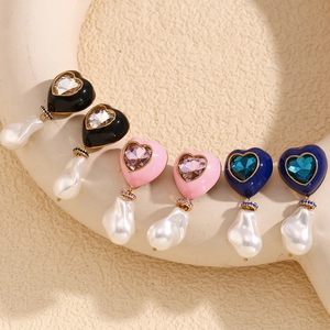 Close-up of heart-shaped earrings with colorful stone inlay and baroque pearls in 18k gold